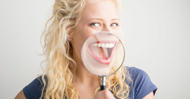 Woman with a magnifying glass over her open mouth, smiling